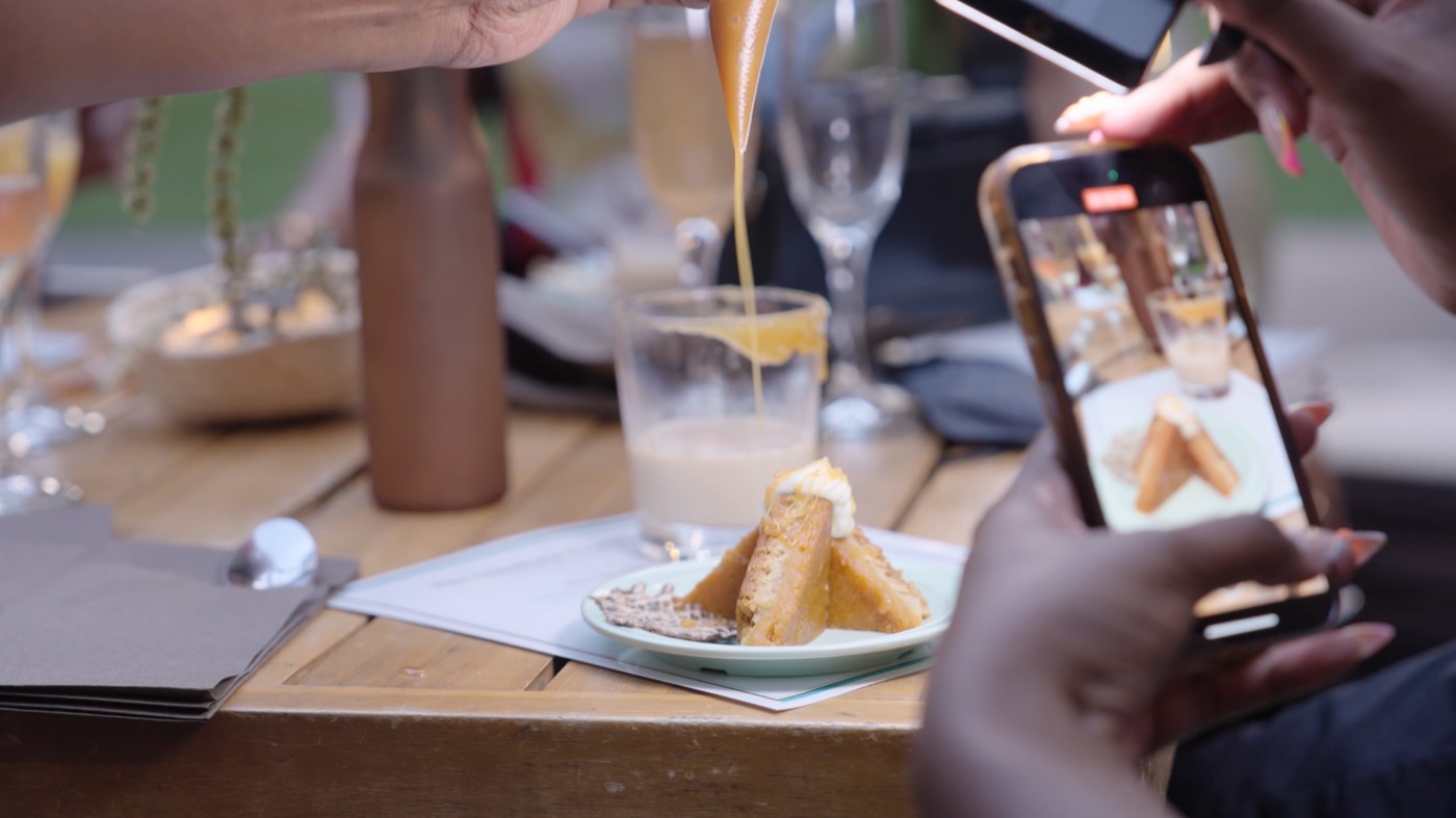 Caramel is poured over a plated dessert while guests film it on their phones.