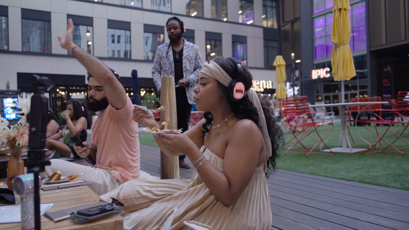 A guest in headphones tastes a course at the outdoor table at golden hour.