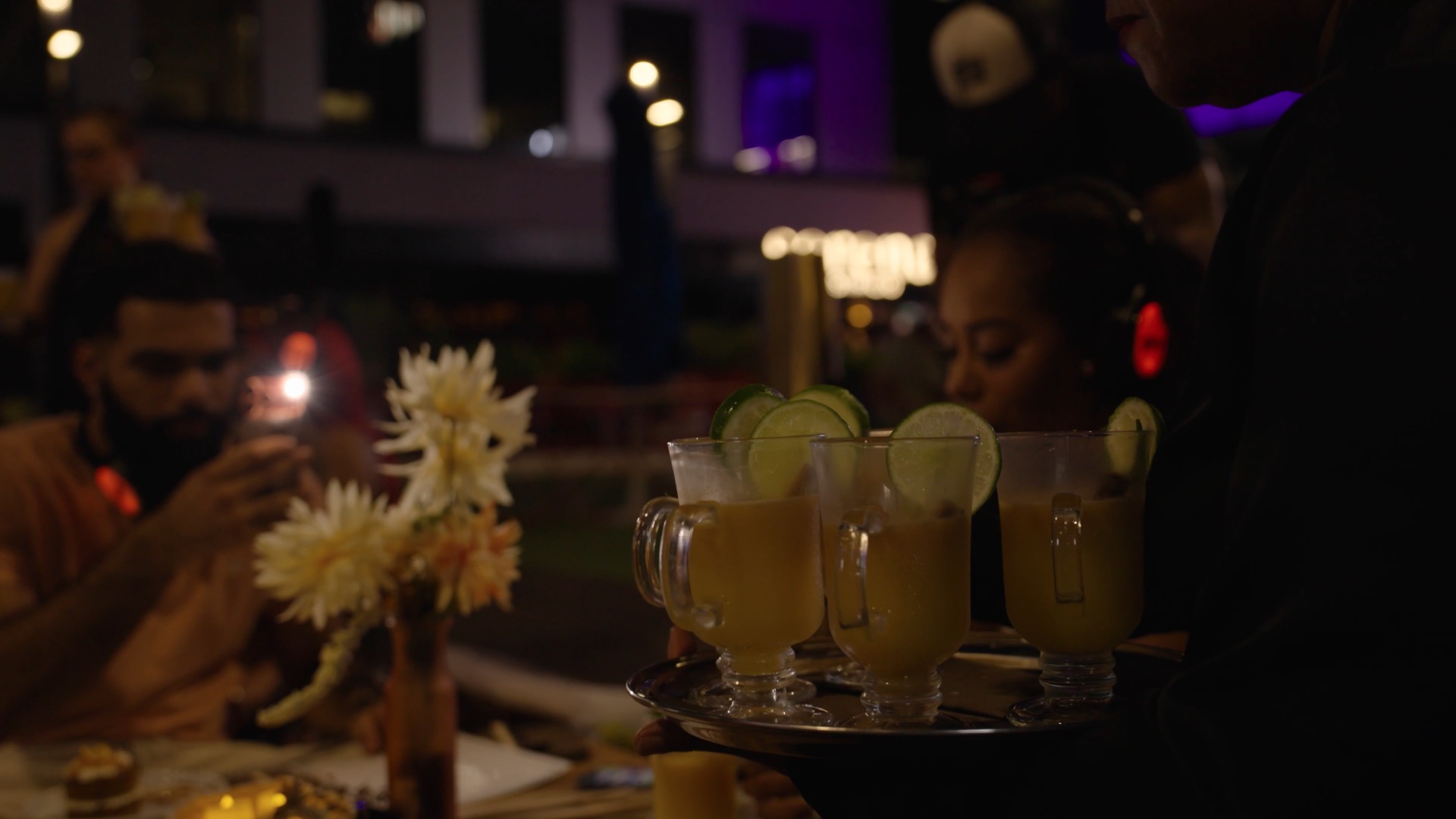 A server carries a tray of citrus cocktails through the candlelit table at dusk.