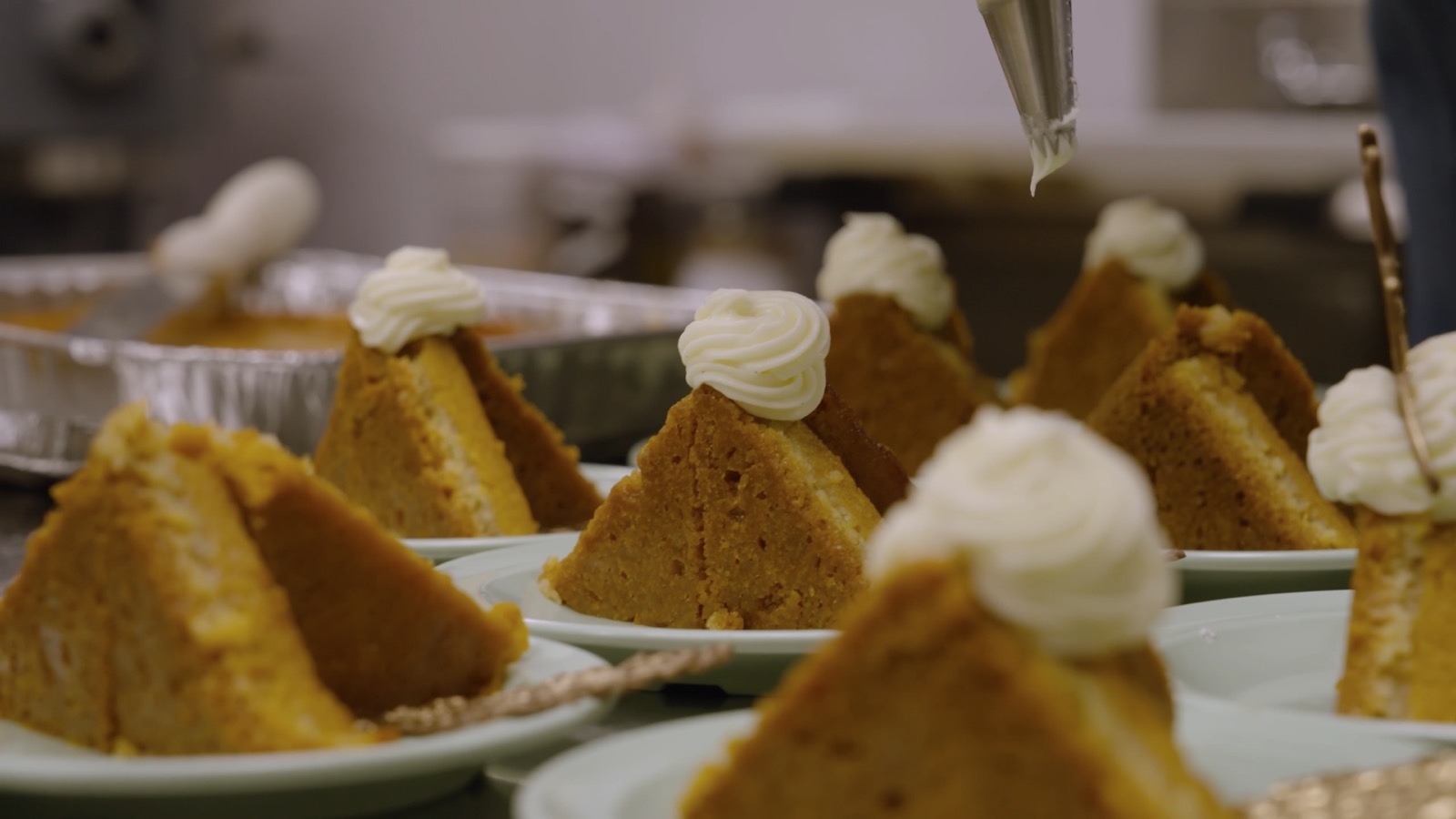Sweet potato pie slices plated in a row, each finished with a piped rosette of cream.